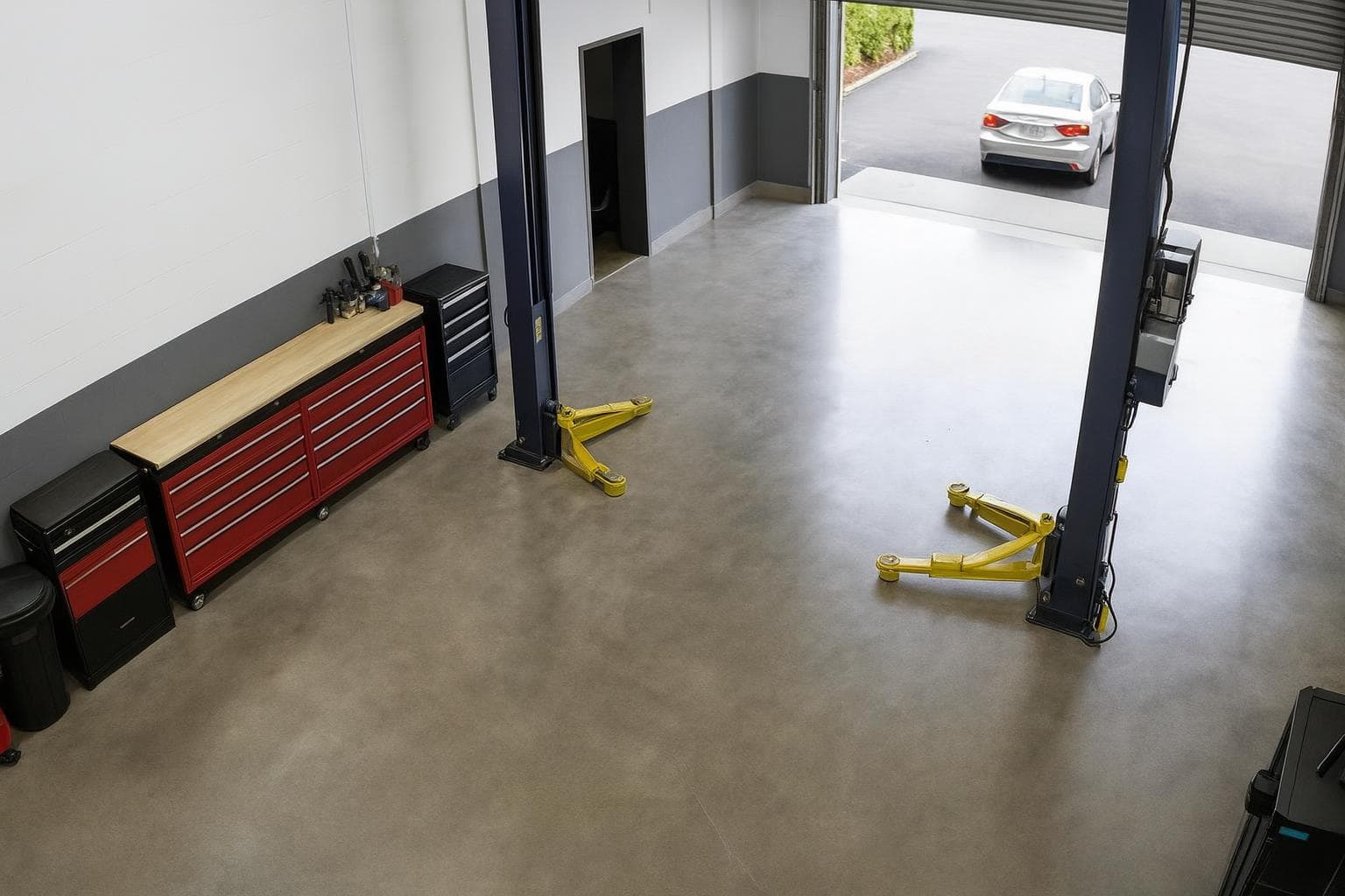 The bay floor empty between the lift posts as the sedan drives away outside the roller door