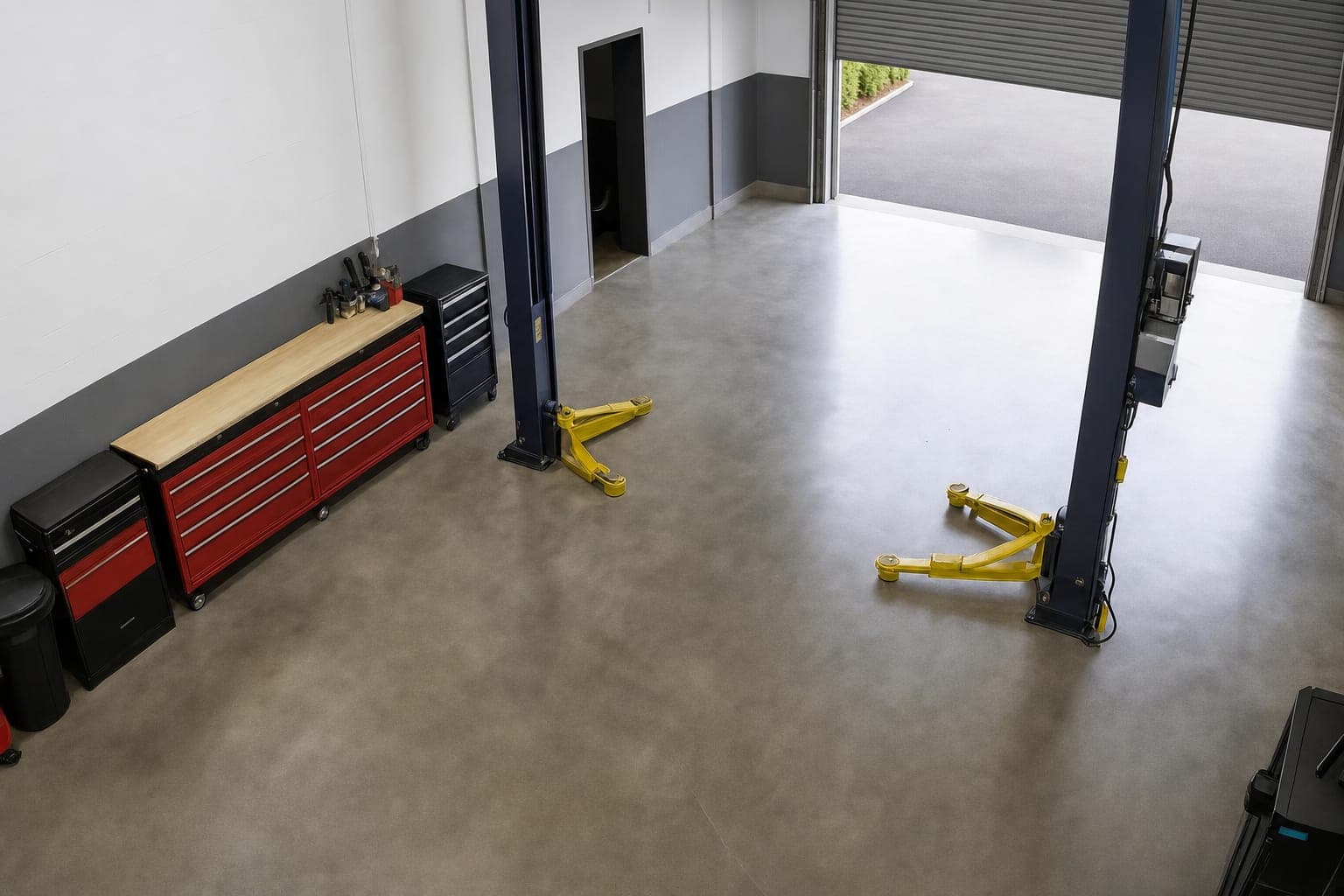 Service bay camera view of the roller door partway up over an empty driveway, the bay floor clear