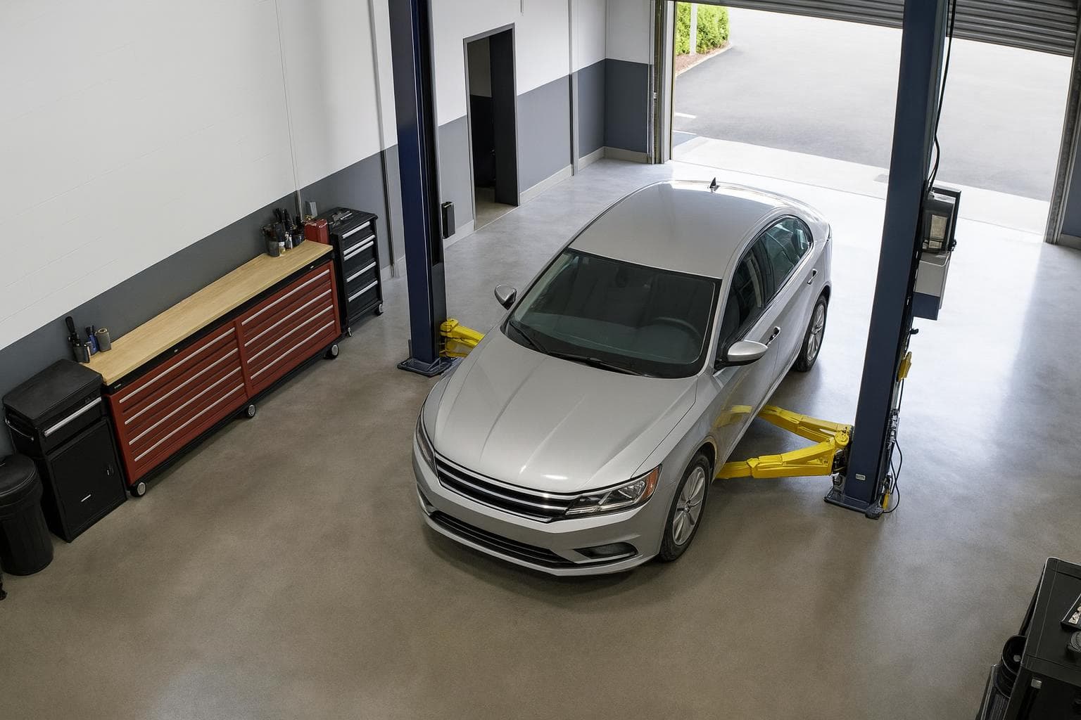 The same bay with the sedan still between the lift posts, hood closed and nobody at the car