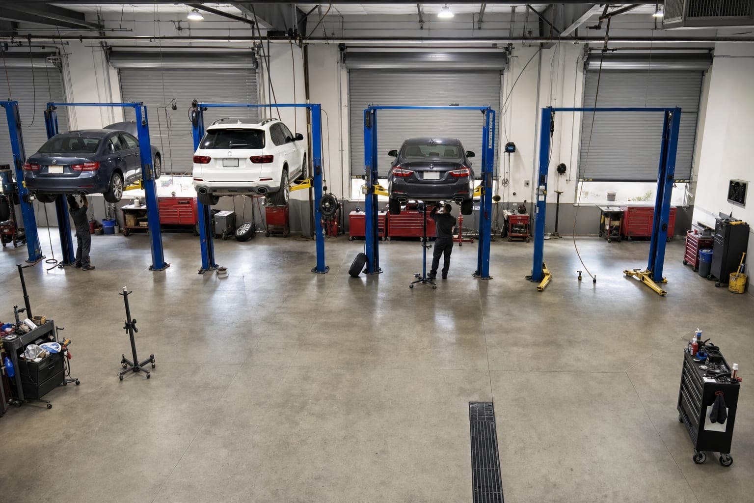 Overhead view of a four-bay repair shop, three cars up on lifts with technicians under two of them and one bay empty