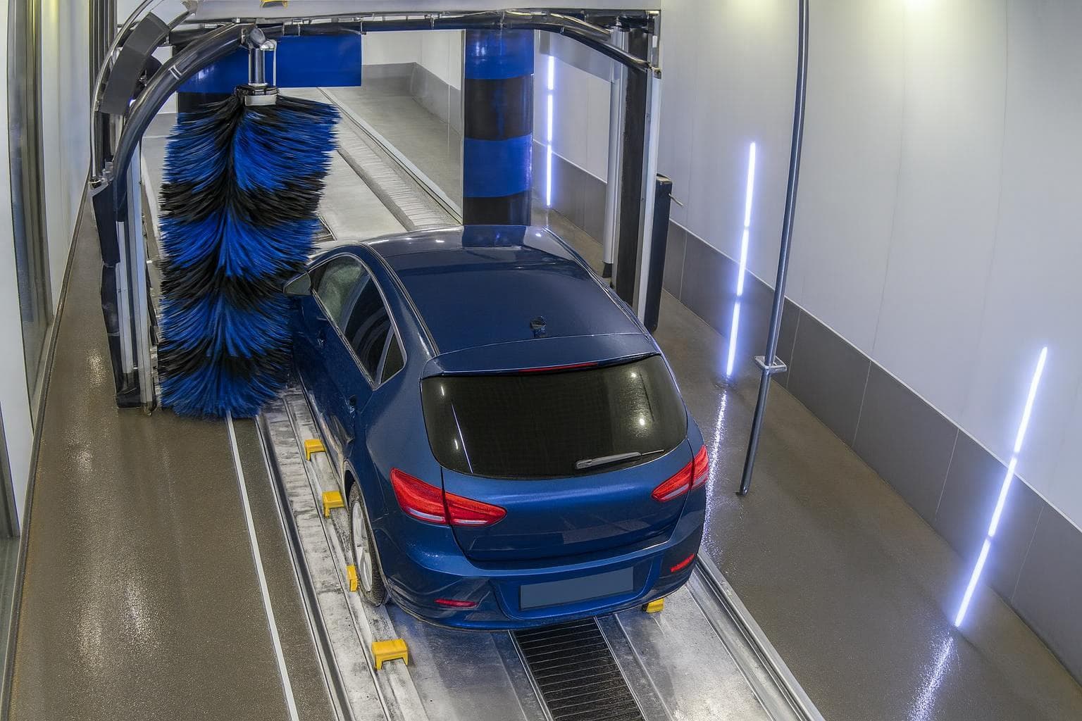 Tunnel camera view of a dry blue hatchback on the conveyor, just short of the brushes